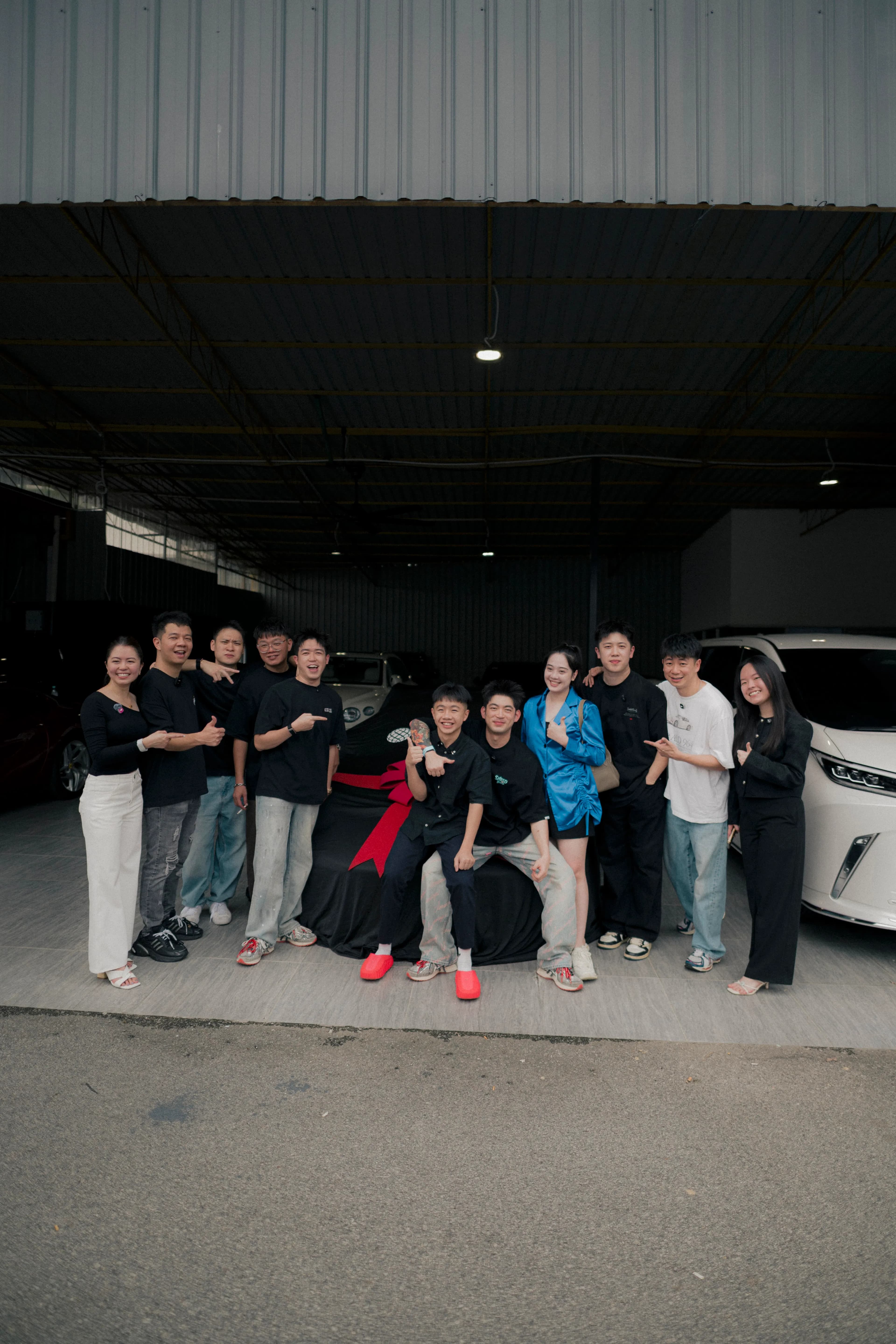 D&Dream team gathered around a car under a black cover with a red bow